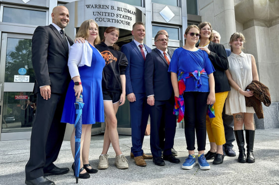 Two teens challenging New Hampshire's new law banning transgender girls from girls' sports teams, Parker Tirrell, third from left, and Iris Turmelle, sixth from left, pose with their families and attorneys in Concord, N.H., Monday, Aug. 19, 2024.