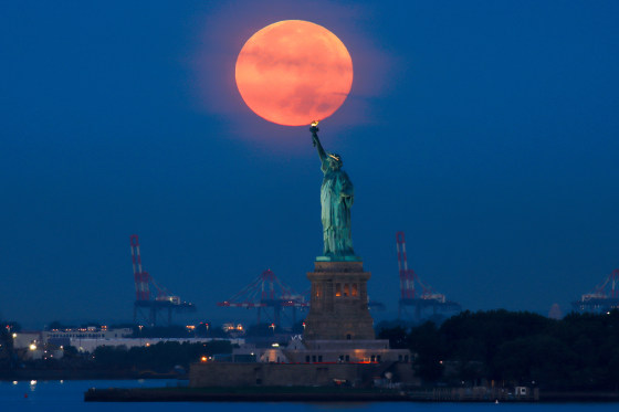 Full Harvest Moon Sets at Sunrise, the flame of the Statue of Liberty appears to touch the bottom of the moon in the sky