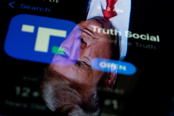 An image of former President Donald Trump reflected in a phone screen that is displaying the Truth Social app