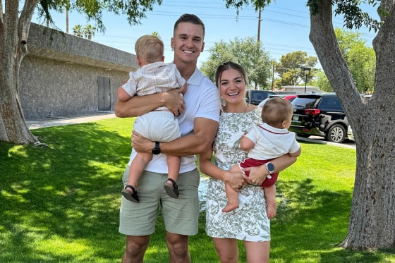 Matt and Abby Howard pose for a portrait outside on a lawn with their two children.