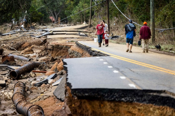 People walk across a damaged road with pipes exposed through the concrete