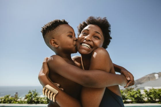 Boy kissing on cheeks of her mother. Cute boy hugging his smiling mother and kissing in her face.