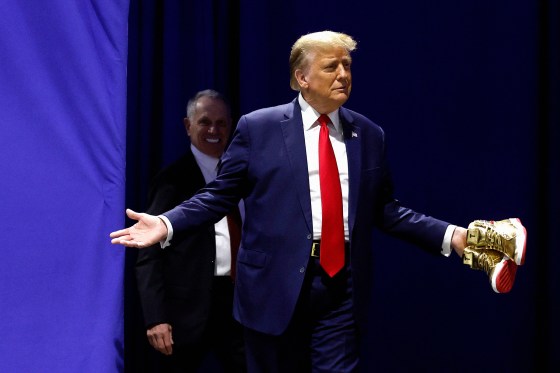 Donald Trump holding a pair of gold sneakers against a blue background