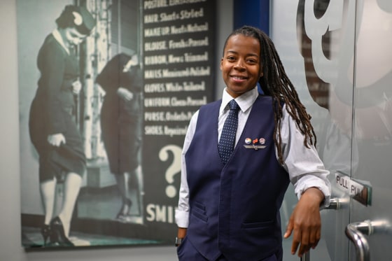 Keturah Johnson poses by a decades old, outdated poster with rules and uniforms for flight attendants,