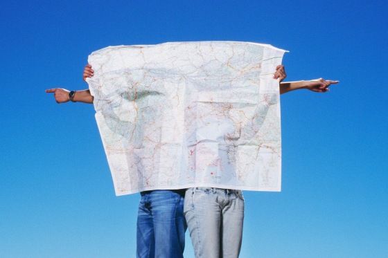 Two people behind a paper map and pointing in opposite directions against a blue sky.