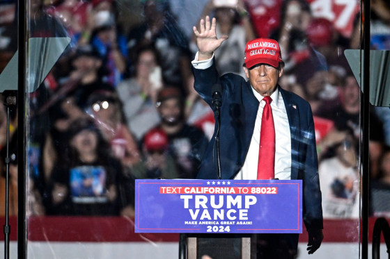 Donald Trump waves on stage behind protective glass