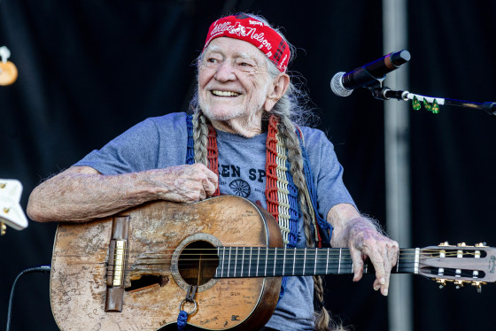 Willie Nelson holding a guitar while seated on stage