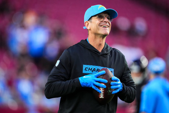 Jim Harbaugh smiles and holds a football on the field