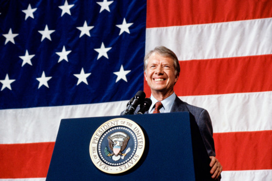 Jimmy Carter smiles at a podium with the american flag behind him