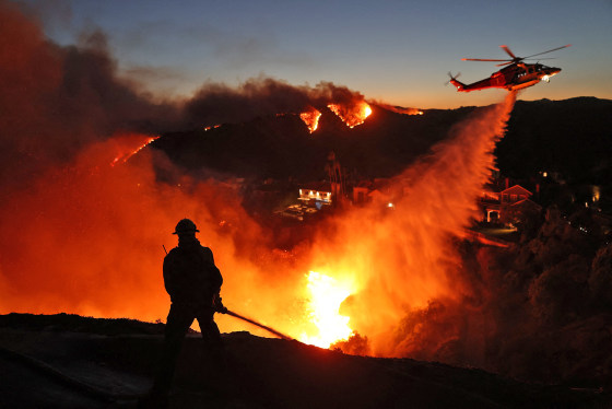 A helicopter drops water as the Palisades Fire grows