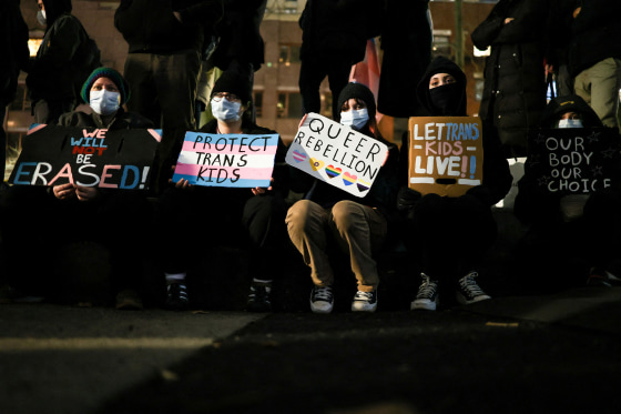 People sit on a curb and hold signs in support of LGBTQ rights