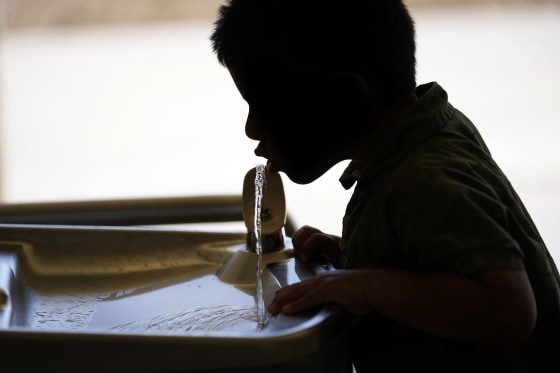 A silhouette of a child drinks from a water fountain