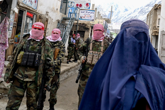 Taliban fighters stand guard as a burqa-clad woman walks along a street