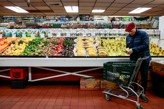 A person holds bananas near their shopping cart in the produce section of a grocery store