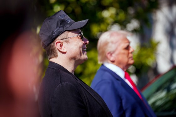 Elon Musk smiles standing next to Donald Trump