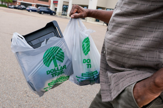 A person walks outside in a parking lot holding two plastic Dollar Tree brand bags filled with items