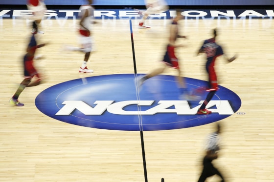 Players dribble the ball on the NCAA logo at half court