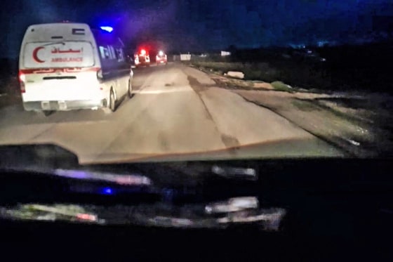 A Red Crescent ambulance with its emergency lights flashing drives toward a fire truck and other ambulances in Rafah, Gaza