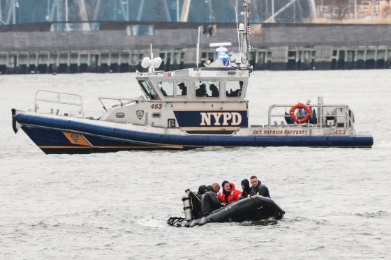 A scuba team rides in an inflatable boat in a river in front of an NYPD boat