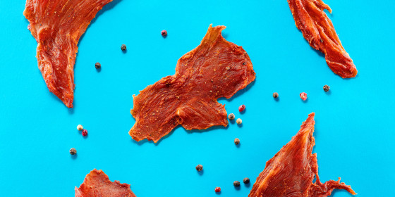 pieces of meat jerky with pepper on bright blue background