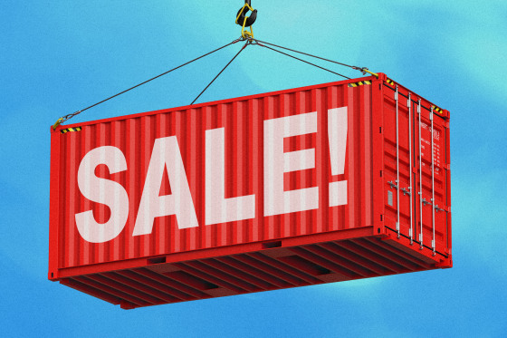 Large red shipping crate being lowered by a crane. The word "Sale!" is painted across the side of the crate in white letters.