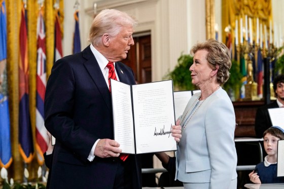 Donald Trump, left, holds a signed executive order folder open, and Linda McMahon stands to his right, looking at each other
