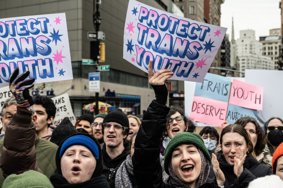 Demonstrators hold signs that read, "Protest Trans Youth."