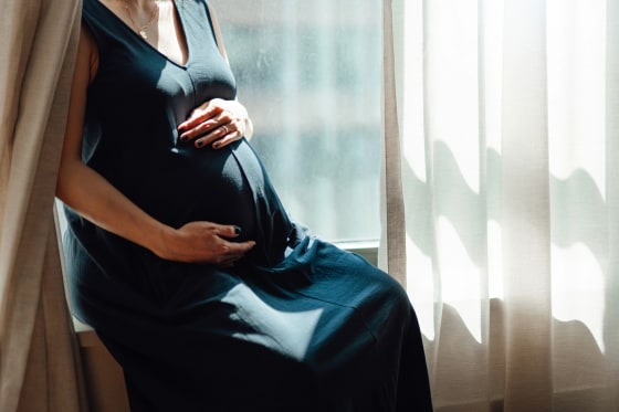 Pregnant Woman Touching Her Belly While Sitting On Window Ledge