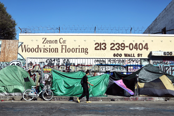 A person walks past an encampment of unhoused people in the Skid Row community on in Los Angeles.