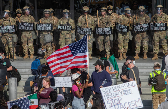 Demonstrators holding signs and flags face California National Guard members standing guard outside the Federal Building