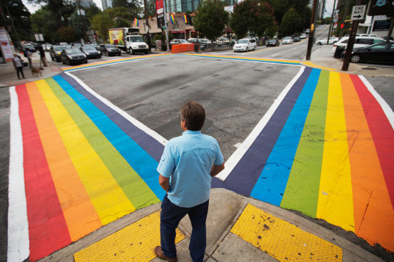 A pedestrian waits to cross a rainbow painted crosswalk