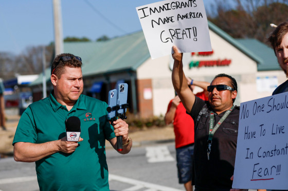Mario Guevara holds a microphone and records with two phones outside next to protestors