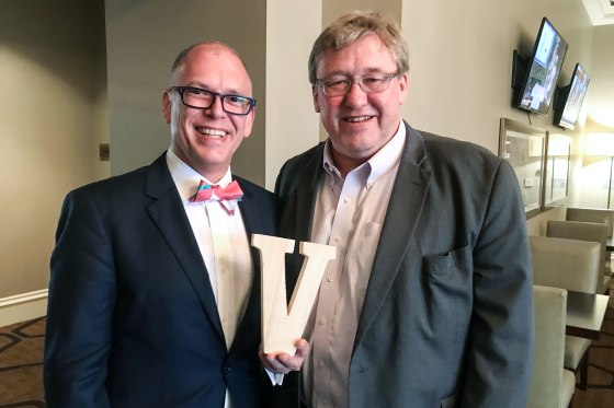 Jim Obergefell, left, and Rick Hodges stand together for a photo in a lobby, Jim holds a wooden letter V between them