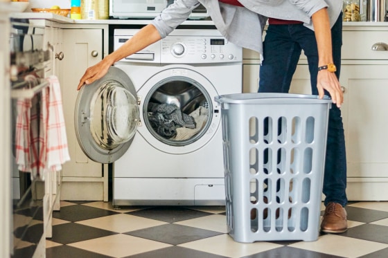 Young man doing laundry in washing machine in his kitchen