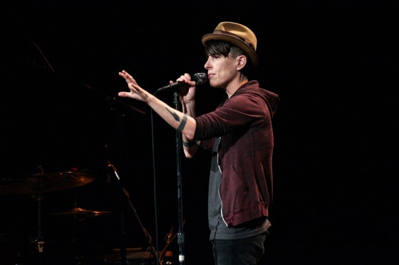 Andrea Gibson speaks into a microphone while standing on stage, one arm outstretched