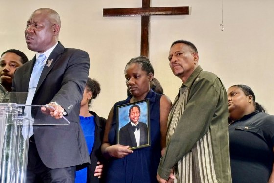 Ben Crump speaks to reporters as Jabari Peoples' parents stand behind him holding a photo of their son.