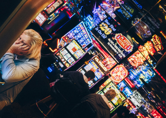 A woman holds her hand in her face while sitting at a slots machine.