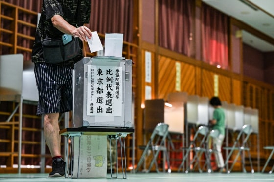 A person puts a ballot in a ballot box inside of a polling station