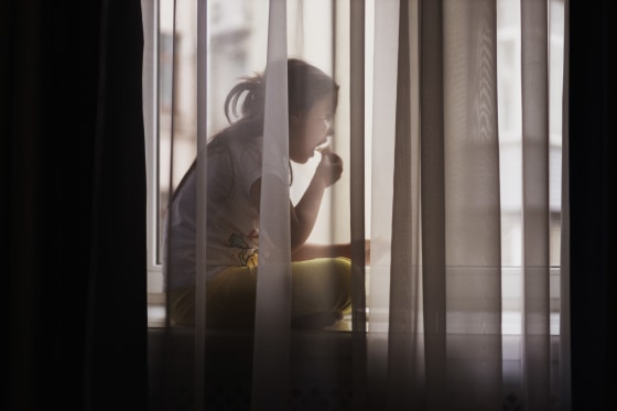 Small girl in white t-shirt and yellow leggings sits on window sill, indulging in quiet snack