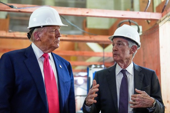 Donald Trump and Jerome Powell stand next to each other wearing white hard hats, as Jerome speaks