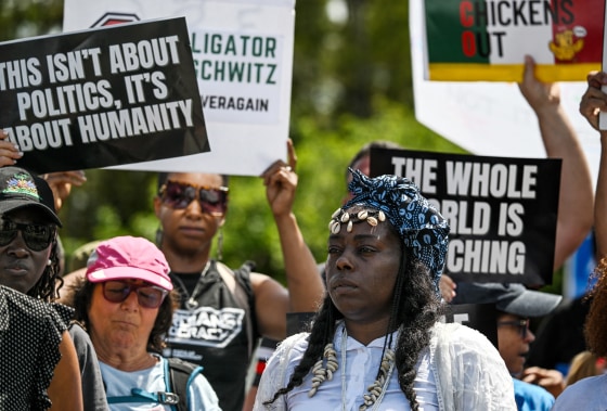 Protesters hold signs that read "This isn't about politics, it's about humanity," and "The whole world is watching."