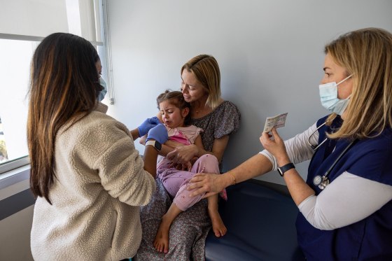 Dr. Neville Anderson, right, tries to cheer up and distract a young patient receiving her DTap Polio and MMR Chickenpox vaccinations in Los Angeles on March 25, 2025.