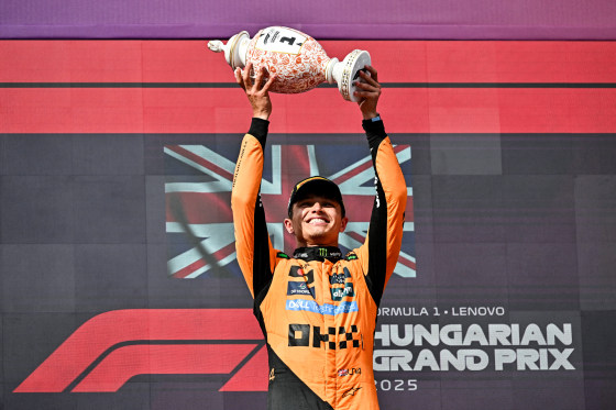 Lando Norris holds a trophy over his head and smiles
