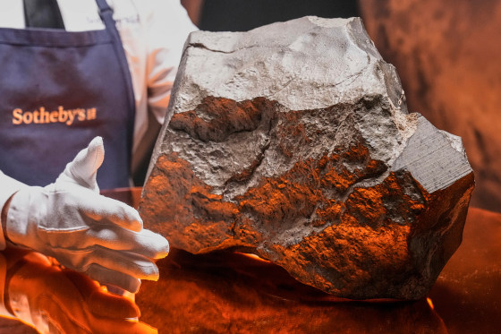 A gloved hand hovers near a rock on a table top