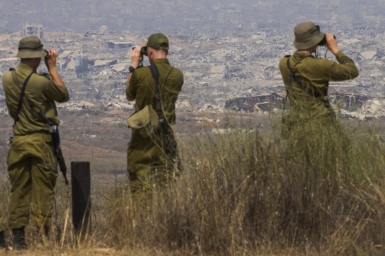 Israeli soldiers uses binoculars to look at damaged buildings in the Gaza Strip, from southern Israel