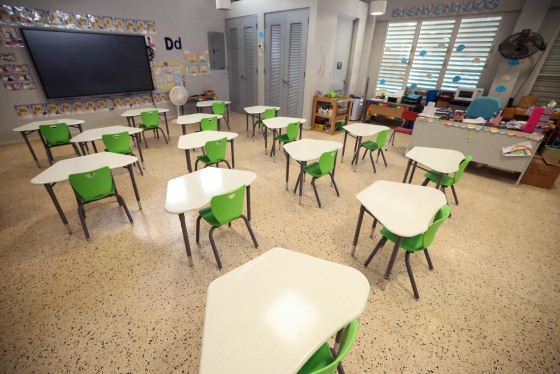 A classroom with desks, a large screen on the left wall, two fans can be seen