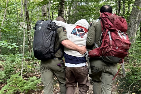Two rangers hold up a person wearing a white hoodie in the forest while walking
