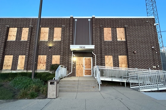 The brick building with windows boarded up with wood planks.