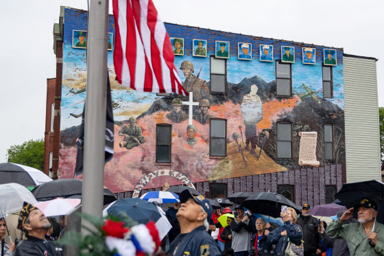Veterans raise a flag in front of the large mural