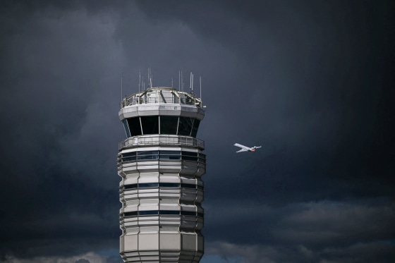 An airplane flies near a control tower on a dark cloudy day